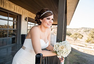 Bride leaning on fence of the barn in the hill country